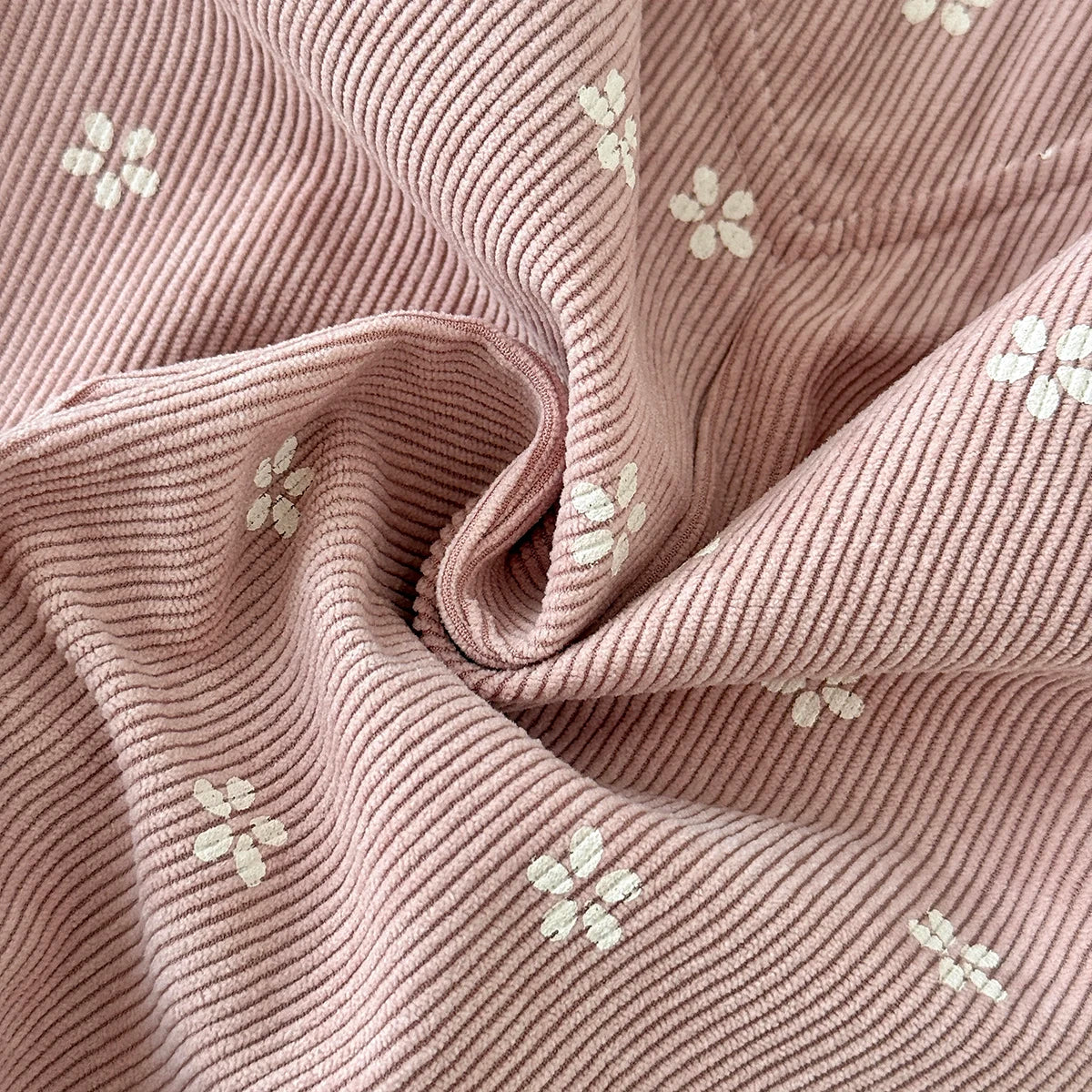 Close-up texture detail of soft pink corduroy fabric with a white ditsy floral print.