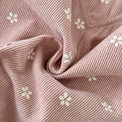 Close-up texture detail of soft pink corduroy fabric with a white ditsy floral print.