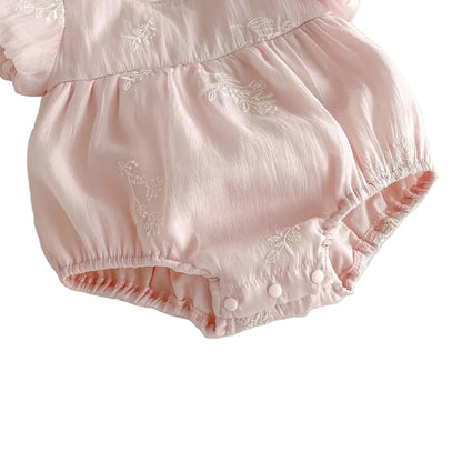 Close-up of white floral embroidery on the dusty pink cotton fabric of a baby girl bubble romper.