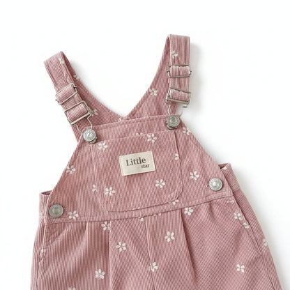 Close-up of the front bib on pink floral toddler overalls, highlighting a Little Star patch and adjustable metal suspender buckles.