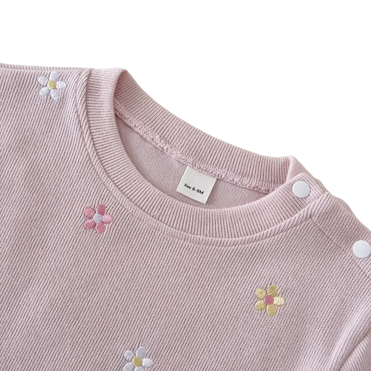 Close-up of the dusty pink crewneck collar showing convenient shoulder snaps and delicate floral embroidery.