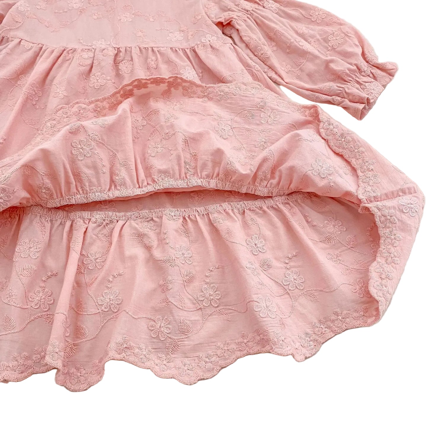 Detailed view of the intricate embroidered scalloped hemline on a pink cotton tiered dress.