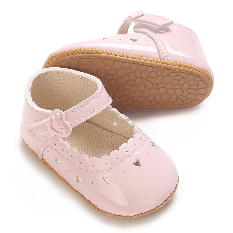 Light pink infant dress shoes showing the side strap and soft shoe bottom.