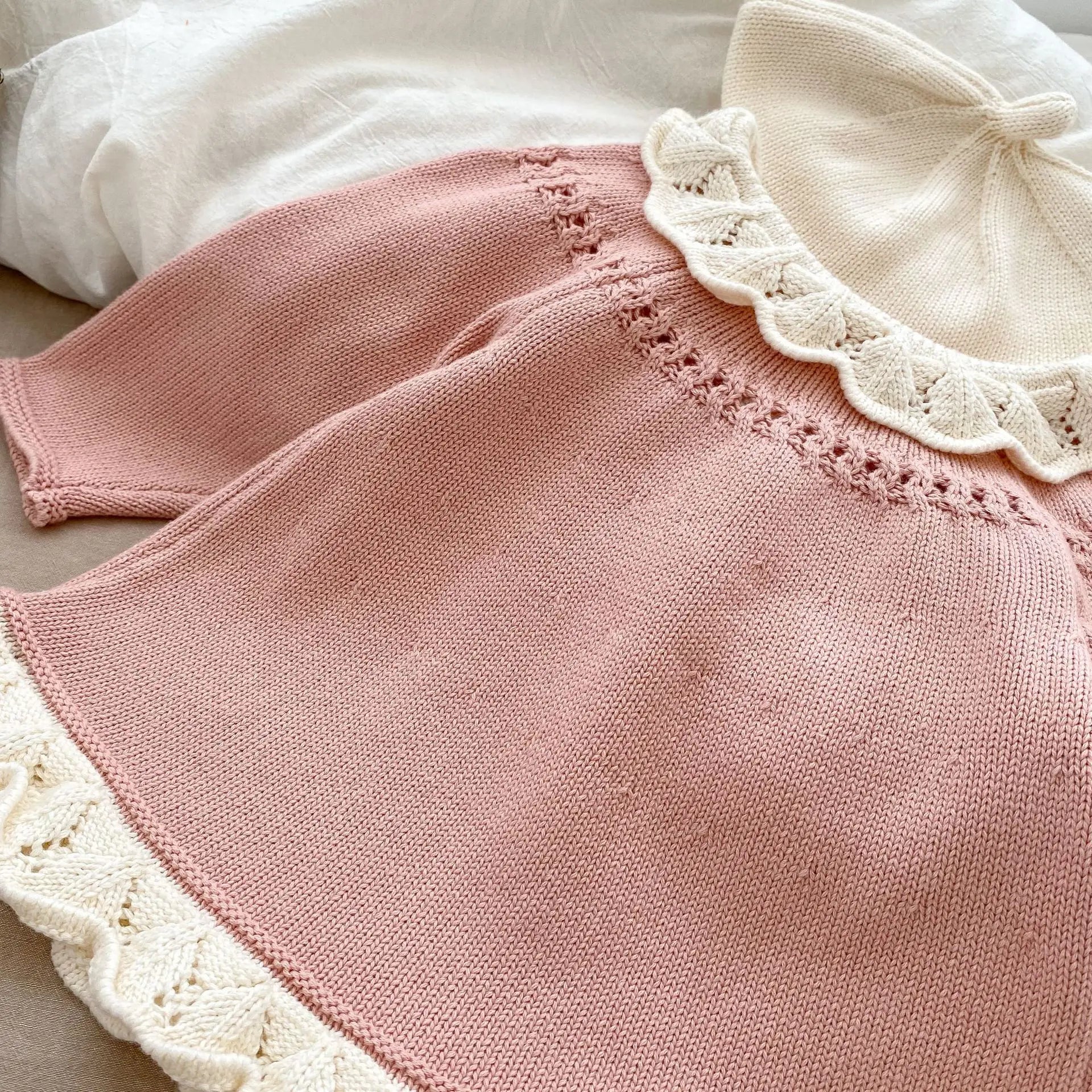 Back view close-up of a pink baby knit cardigan sweater showing the detailed white scalloped lace collar and hemline.