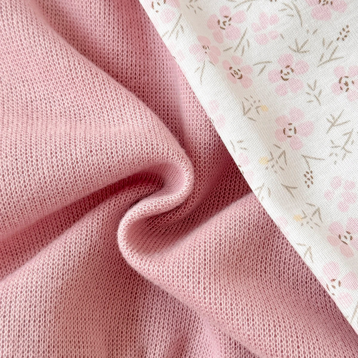 Close-up view showing the soft, high-quality knit texture of the pink sweatshirt fabric side-by-side with the smooth printed floral pants material.