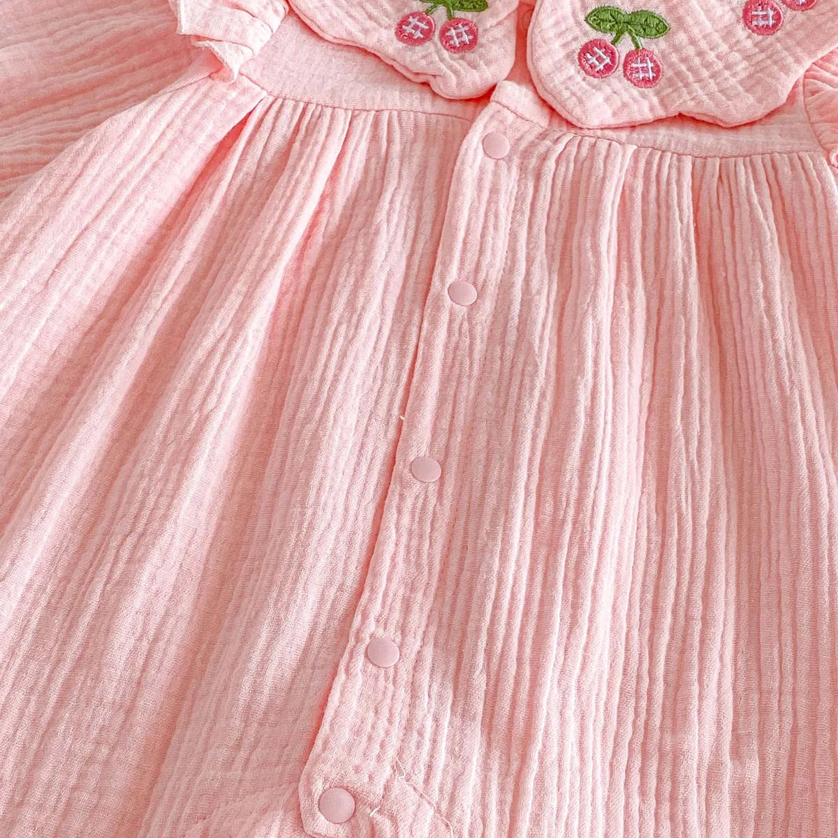 Close-up detail showing the crinkled texture of the pink cotton blend muslin fabric and the row of snap button closures on the front of the Kidsely baby romper.