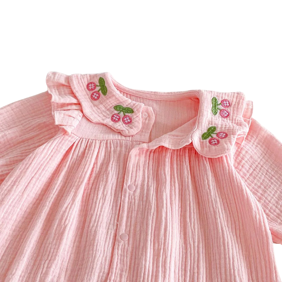 Detailed angled view of the ruffled Peter Pan collar with cherry embroidery on the pink cotton blend muslin romper.