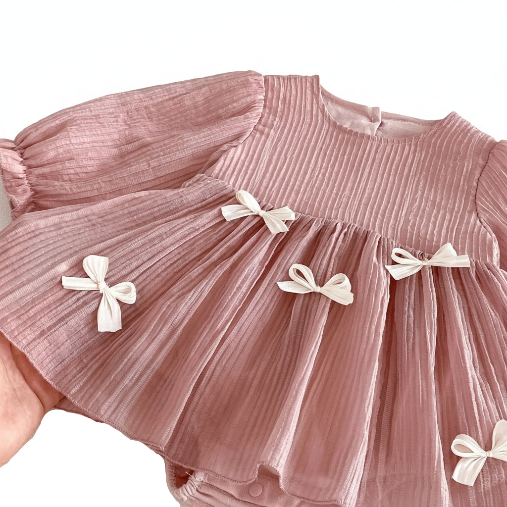 Close-up of the dusty pink baby dress showing the crinkled pleated nylon texture and delicate white bow appliques.