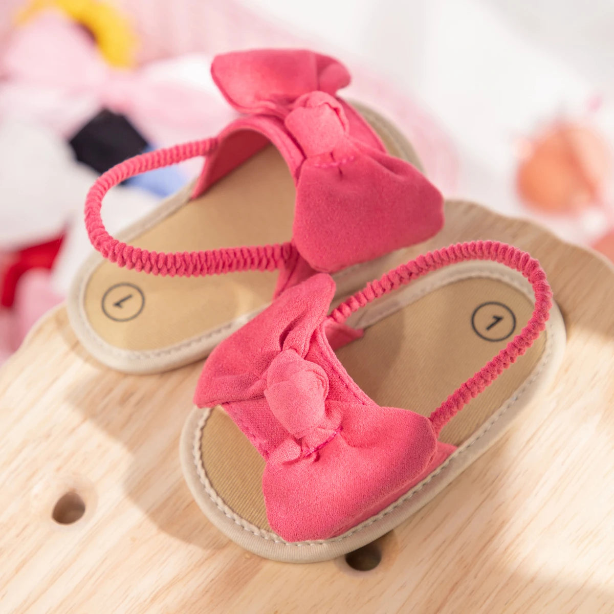 Pink baby girl soft sole bow sandals resting on a natural wood surface.