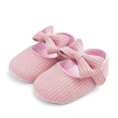 Pair of light pink ribbed knit Mary Jane crib shoes with front bows for baby girls.