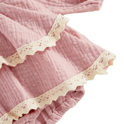 Close-up of the delicate white lace trim on the tiered ruffle hem of a pink textured infant girl romper.