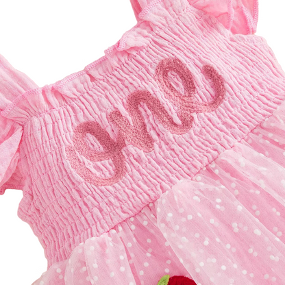 Close-up detail of the pink smocked bodice featuring "one" cursive embroidery and ruffled sleeves.