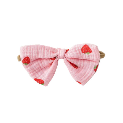 Close-up of the matching pink and red strawberry print pre-tied muslin bow headband.