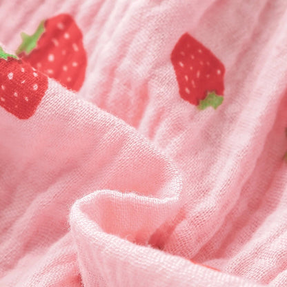 Macro close-up showing the soft, breathable textured pink muslin fabric with printed red strawberries.