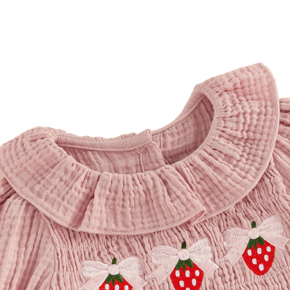 Close-up detail of the ruffled smocked neckline and sweet strawberry embroidery on the pink baby girl romper.