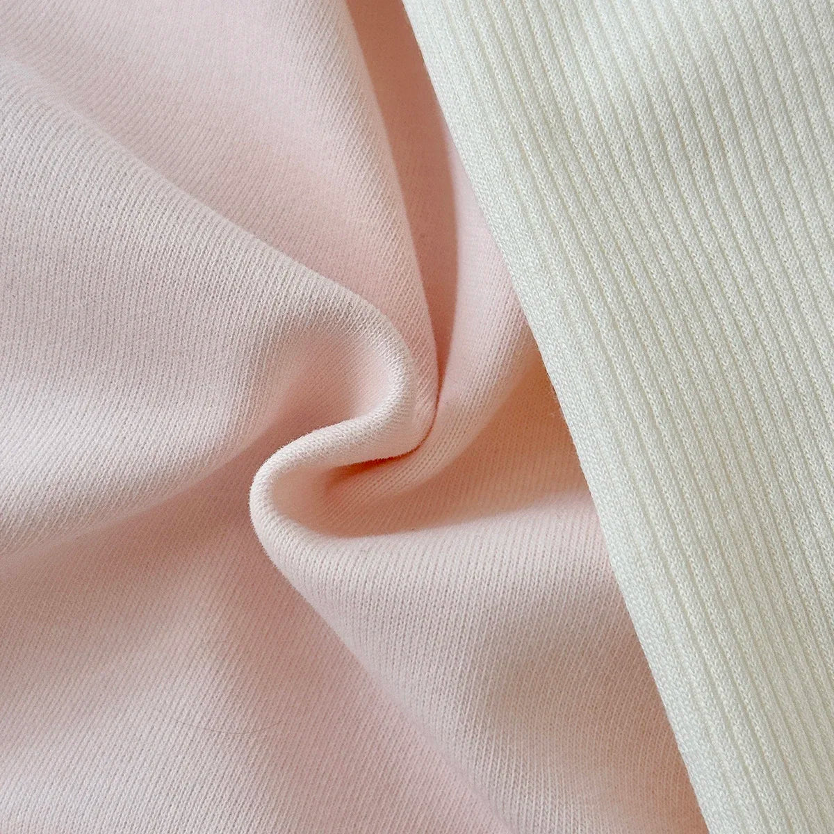 Close-up texture shot showing the smooth pink sweatshirt fabric next to the soft cream ribbed knit leggings fabric.