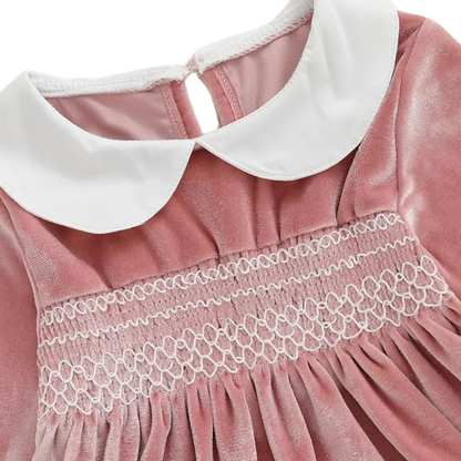 Close-up of white Peter Pan collar and intricate white smocked chest detailing on pink velvet baby romper