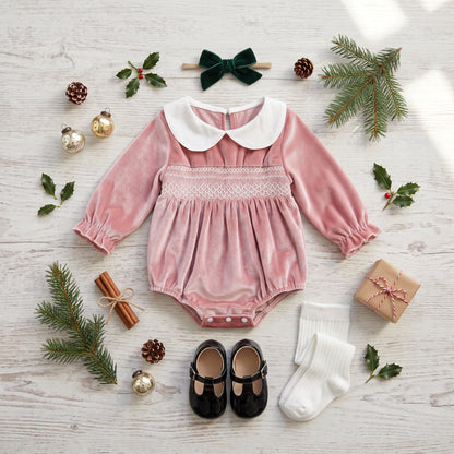 Pink velvet smocked baby bubble romper flat lay with hair bow, socks, and holiday decor
