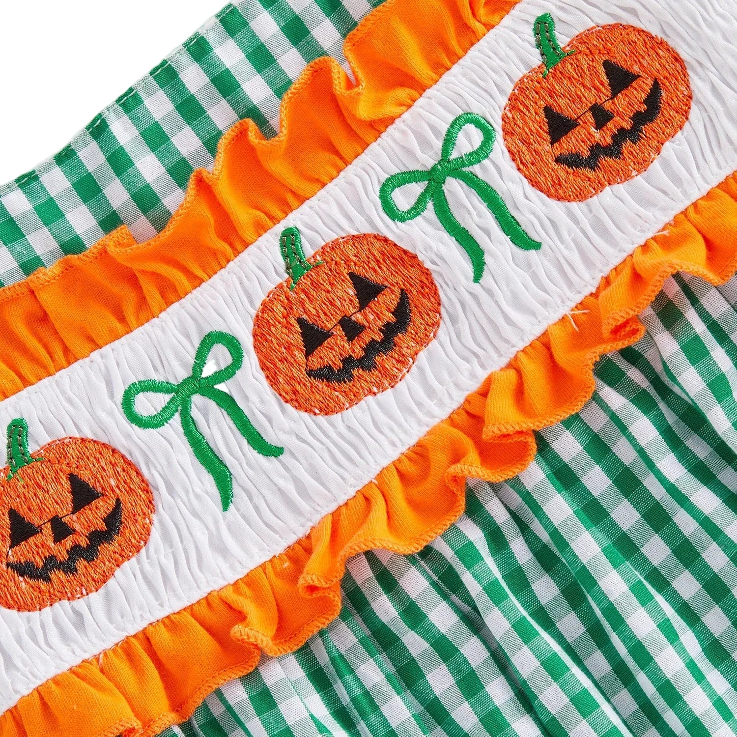 Close up of the detailed hand-smocked jack-o-lantern and green bow embroidery on the chest of the baby girl Halloween outfit.