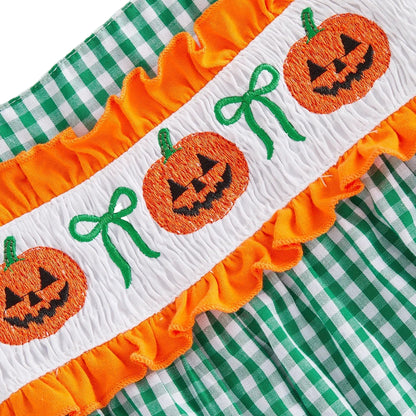 Close up of the detailed hand-smocked jack-o-lantern and green bow embroidery on the chest of the baby girl Halloween outfit.