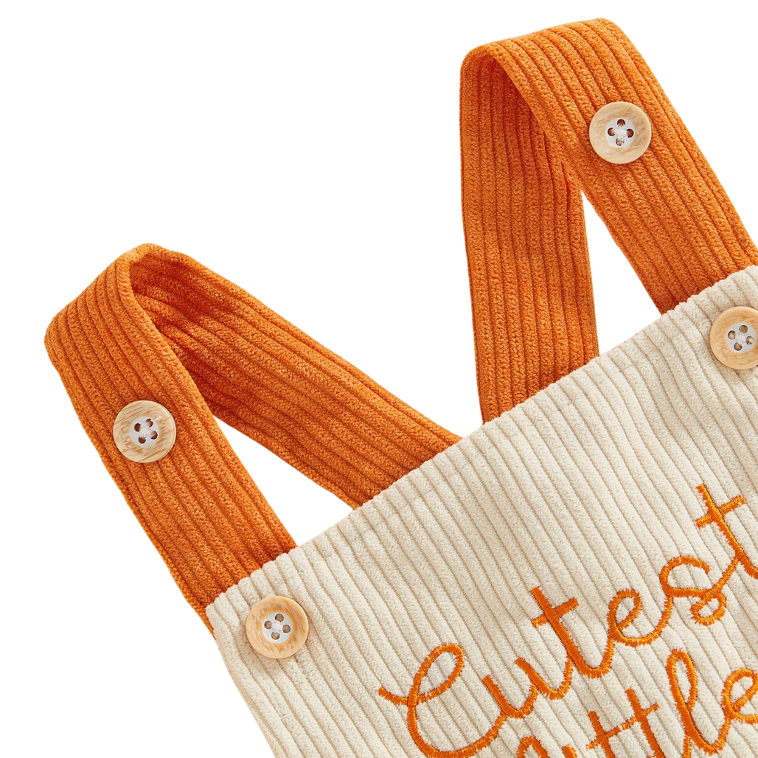 Close-up of the contrasting orange corduroy shoulder straps and button details on the beige baby Halloween jumpsuit.