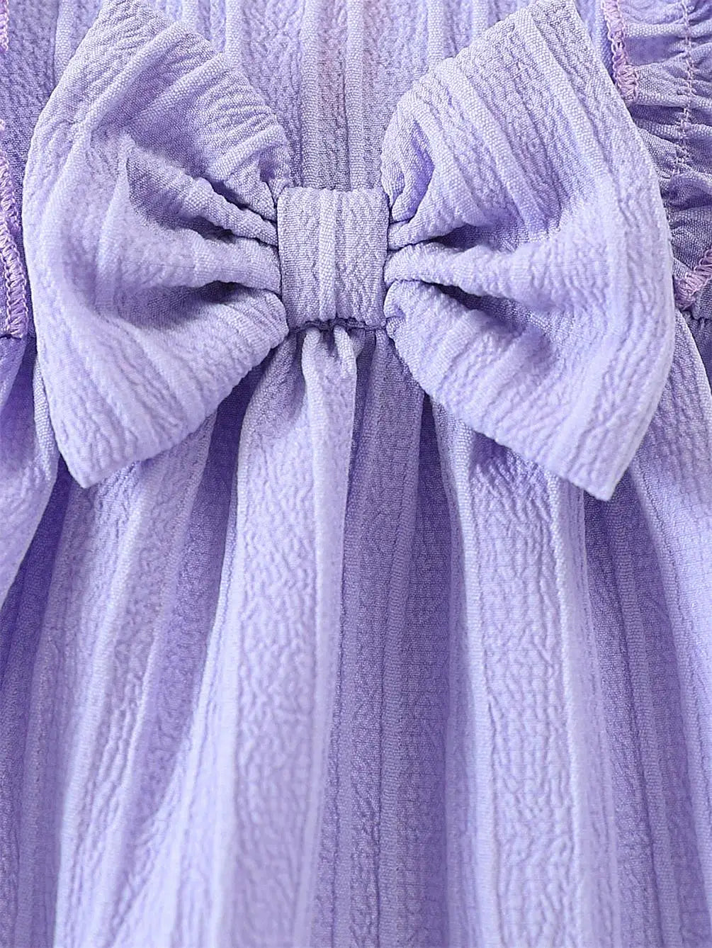 Close up of the classic front bow and ruffled shoulder accents on the light purple baby girl woven sundress.