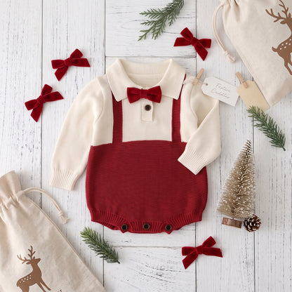 Red and cream baby boy knit holiday romper laid flat on a white wooden background surrounded by festive Christmas props and red bows.