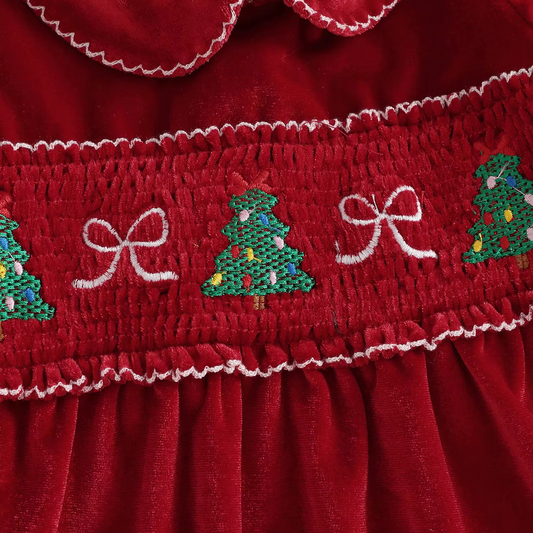 Close-up detail of the smocked chest with embroidered Christmas trees and white bows on a red velvet holiday garment