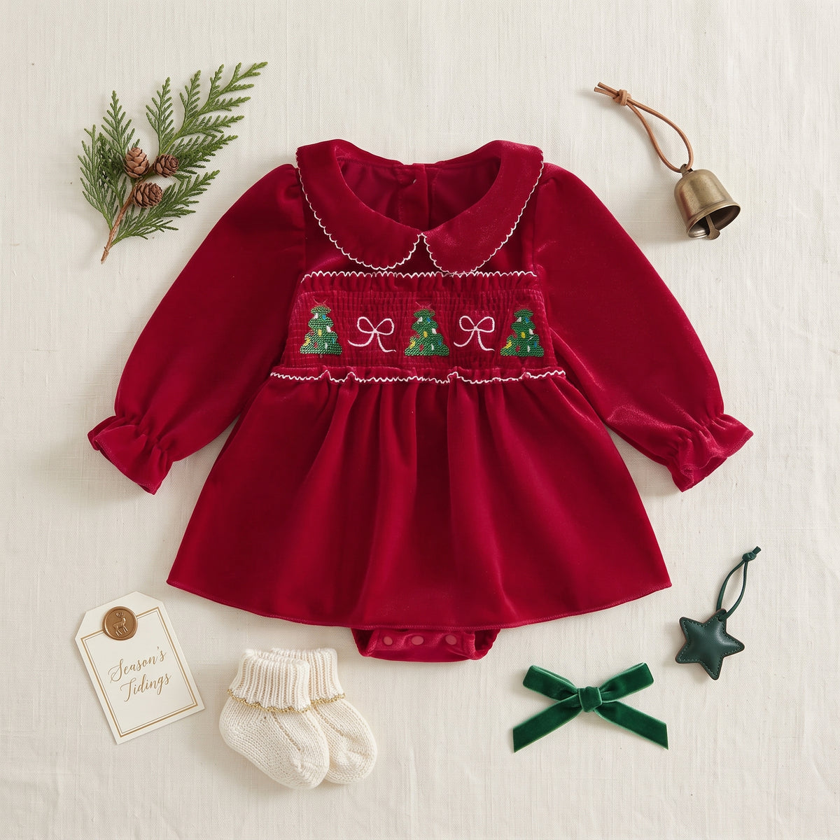 Flat lay of an infant red Christmas bodysuit dress styled with festive pine sprigs and a green bow.