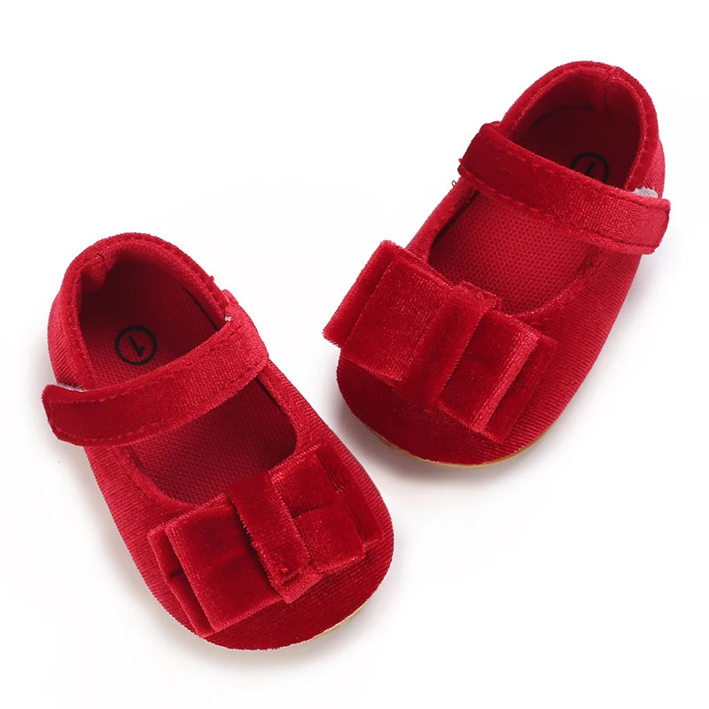 Pair of red velvet baby girl Mary Jane shoes with velvet bow and hook and loop strap