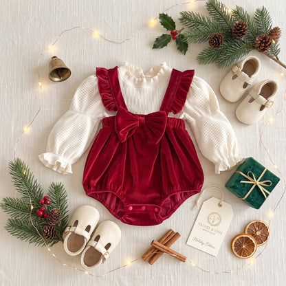 Flat lay view of baby red velvet suspender bubble romper set with holiday pine cone decor.
