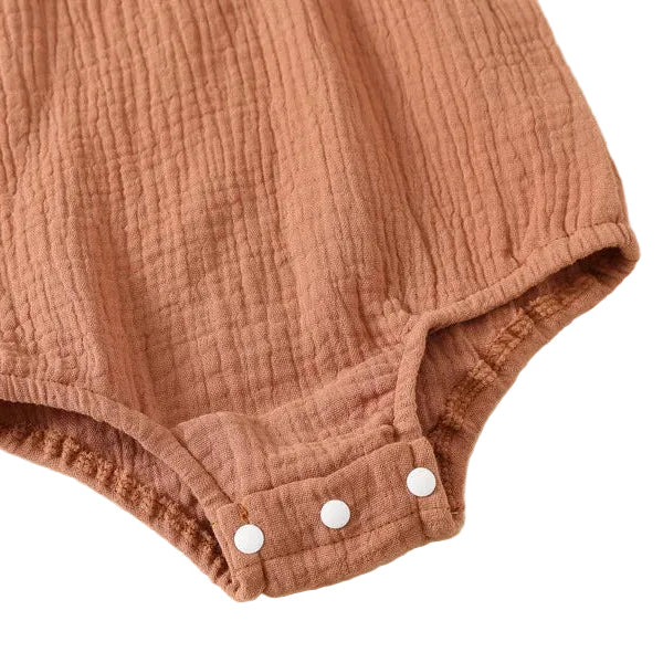 Close-up of the high-tension front triple snap-button closure on the leg opening of a terracotta baby romper for easy diaper changes.