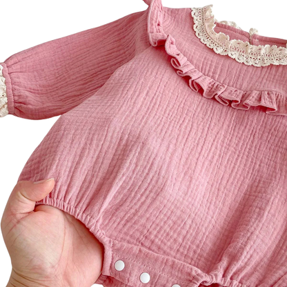 Hand holding the bottom of a pink baby bubble romper showing the reinforced snap button closures designed for easy diaper changes.