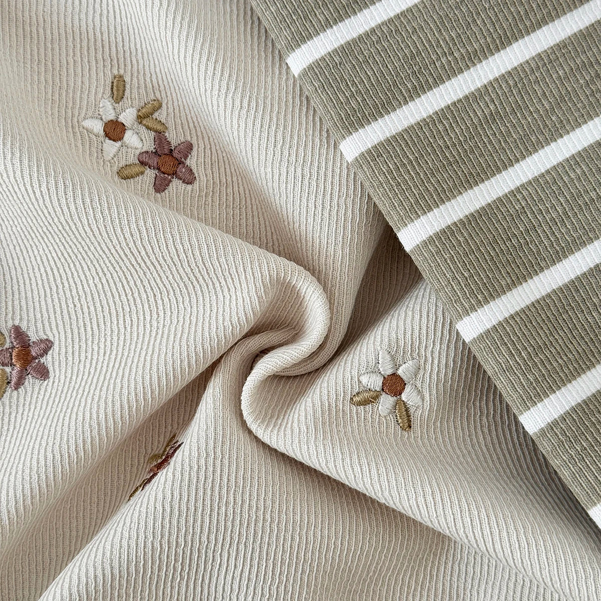 Close-up fabric detail showing the textured cream ribbed knit with embroidered daisies alongside the olive green striped fabric.