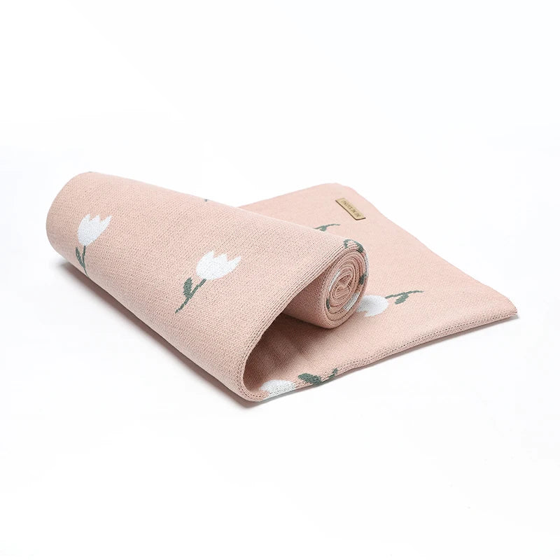 A lightweight blush pink cotton knit swaddle blanket rolled up tightly to demonstrate its compact portability for diaper bags.