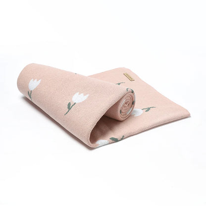 A lightweight blush pink cotton knit swaddle blanket rolled up tightly to demonstrate its compact portability for diaper bags.