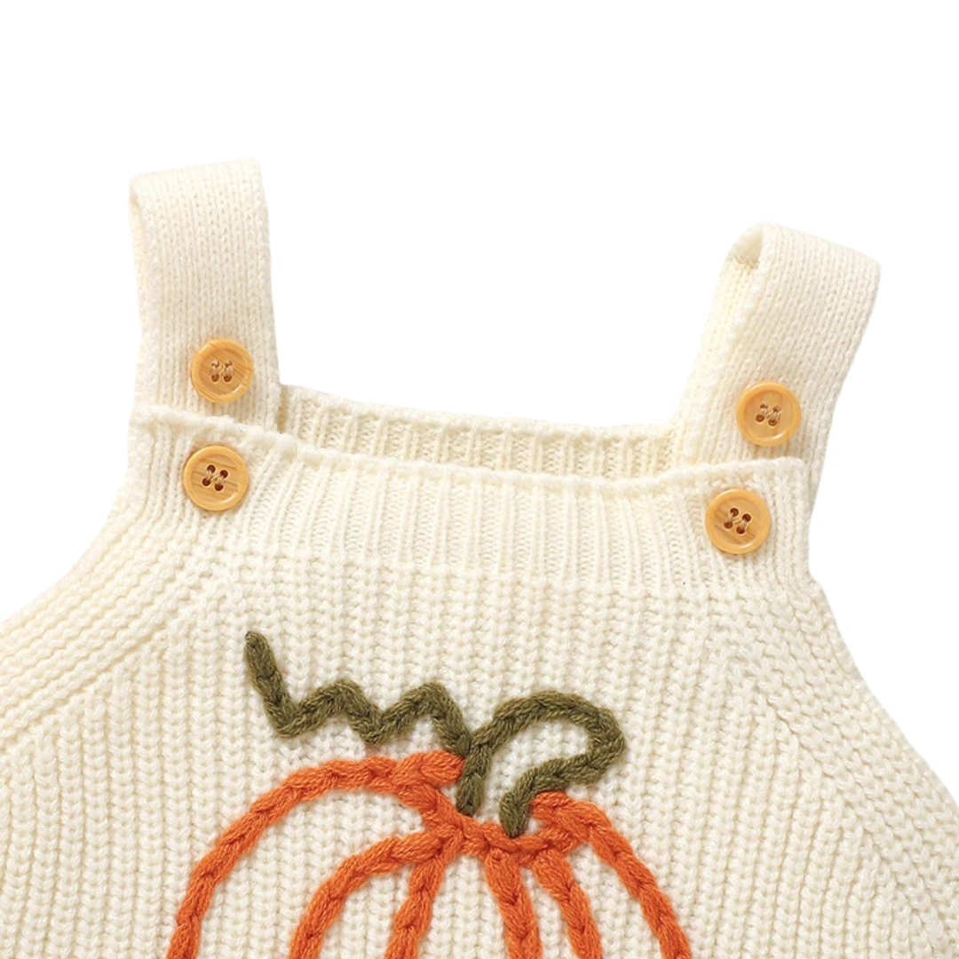Close-up of the upper half of the cream baby knit romper, showing the ribbed chest and buttoned shoulder straps.