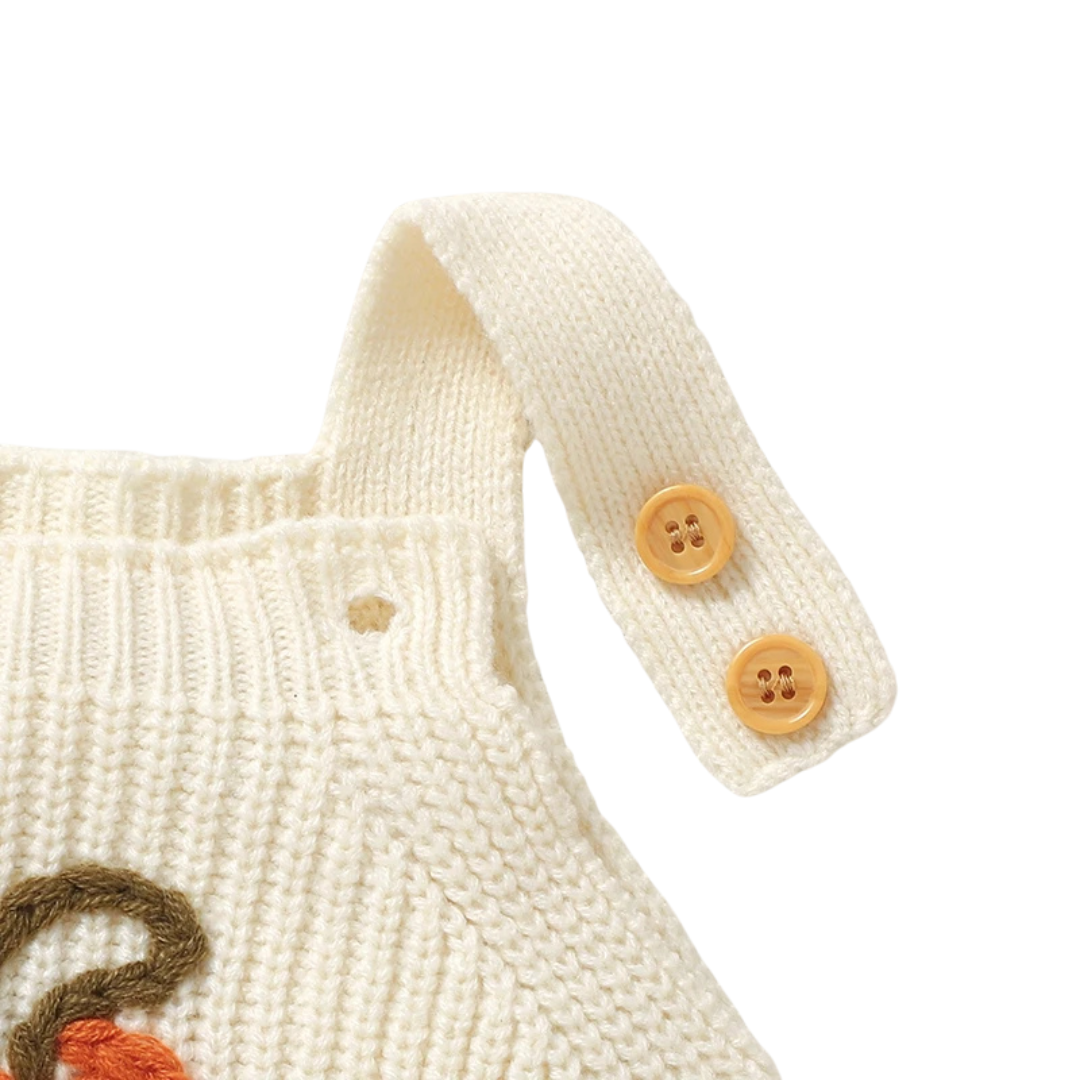 Close-up of an unbuttoned shoulder strap on the cream baby knit romper, displaying the dual buttons for size adjustability.