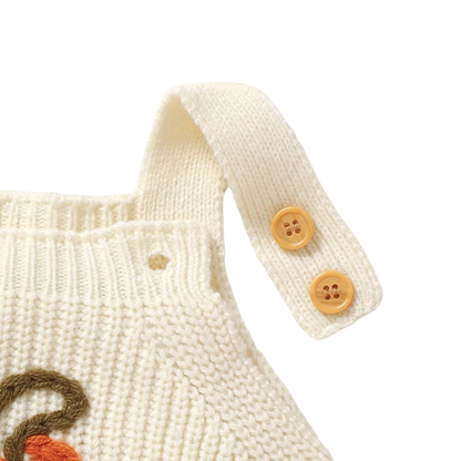 Close-up of an unbuttoned shoulder strap on the cream baby knit romper, displaying the dual buttons for size adjustability.