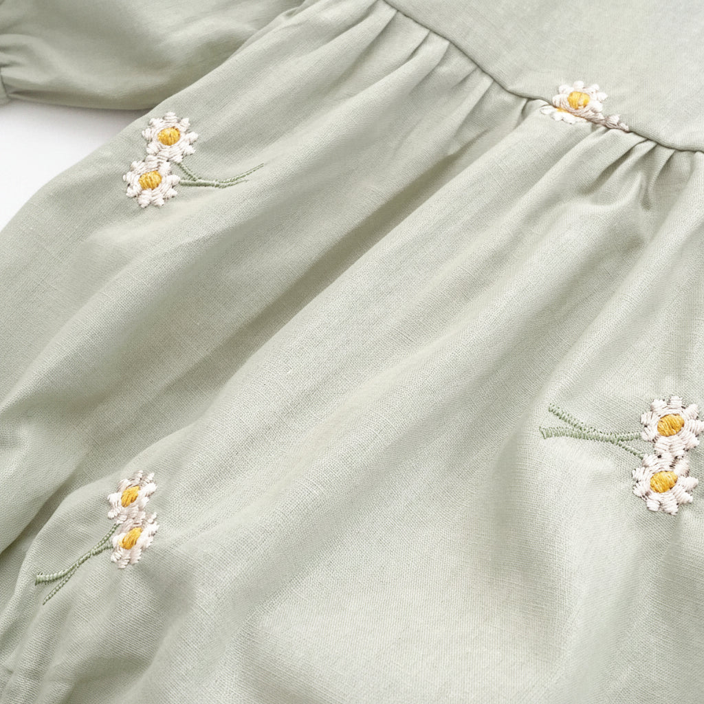 Close-up texture view of the soft sage green cotton blend fabric showing the detailed white and yellow daisy floral embroidery.
