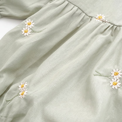 Close-up texture view of the soft sage green cotton blend fabric showing the detailed white and yellow daisy floral embroidery.