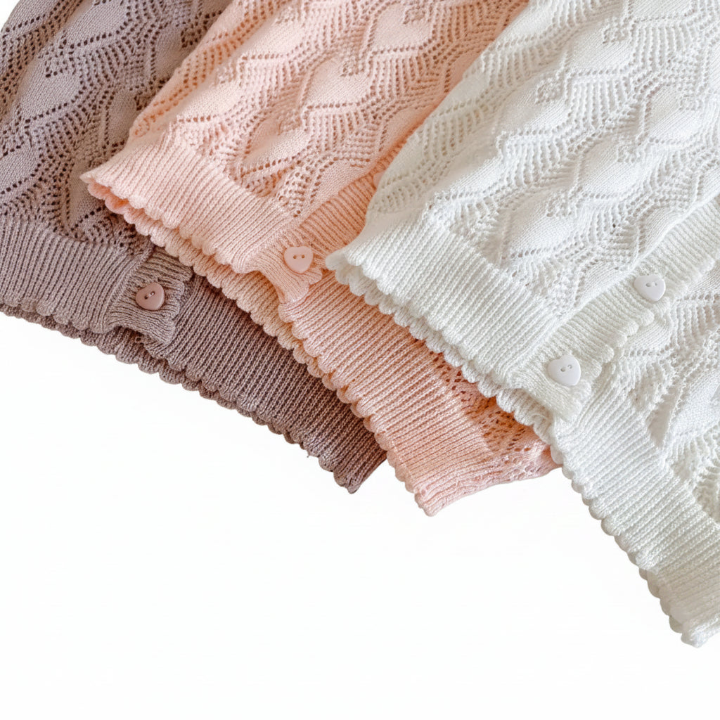 Close-up of the scalloped bottom hems of the mauve, pink, and white pointelle knit baby cardigans lined up together.