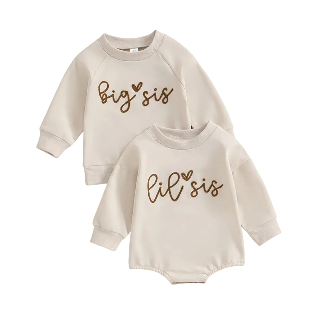 Flat lay of matching neutral cream sister outfits featuring a toddler Big Sis long sleeve sweatshirt and an infant Lil Sis long sleeve romper.