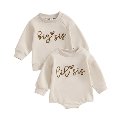 Flat lay of matching neutral cream sister outfits featuring a toddler Big Sis long sleeve sweatshirt and an infant Lil Sis long sleeve romper.