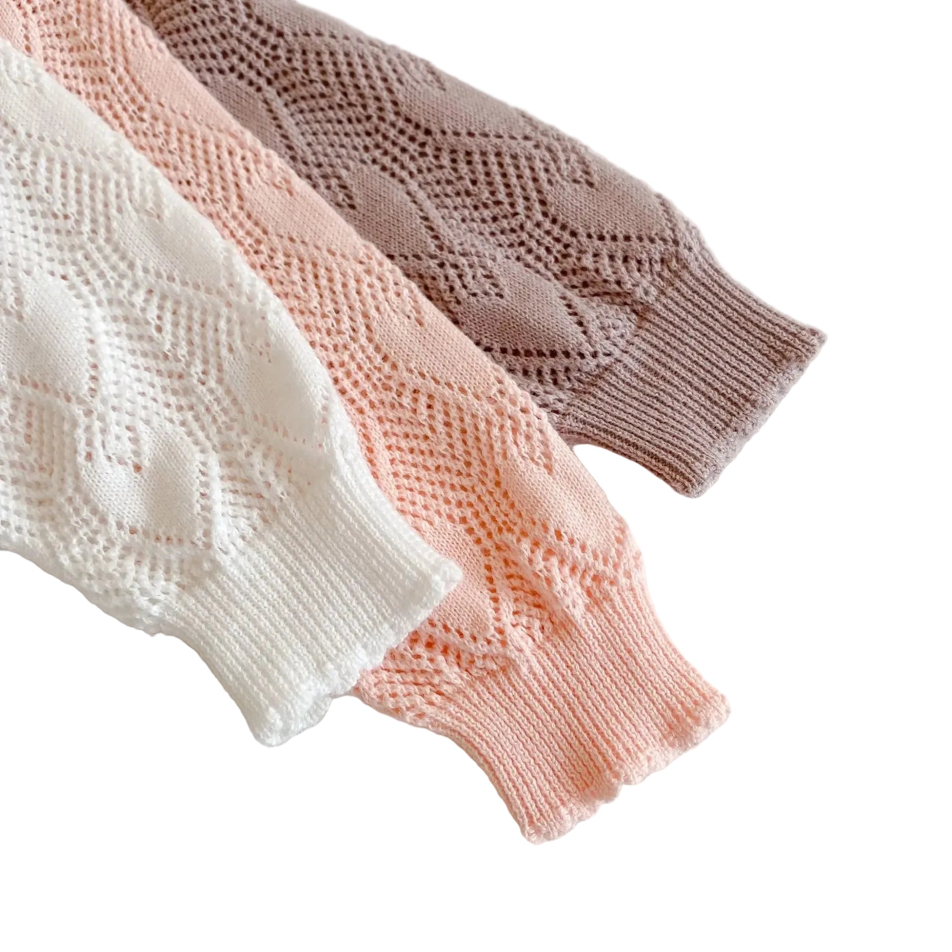 Close-up of the ribbed sleeve cuffs on the white, pink, and mauve baby girl knit cardigans resting next to each other.