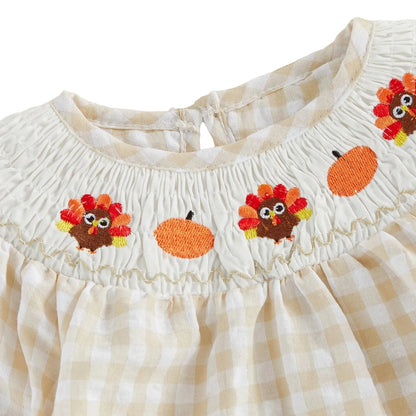 Close-up of the traditional bishop smocked neckline featuring embroidered turkeys and pumpkins on a beige gingham romper.