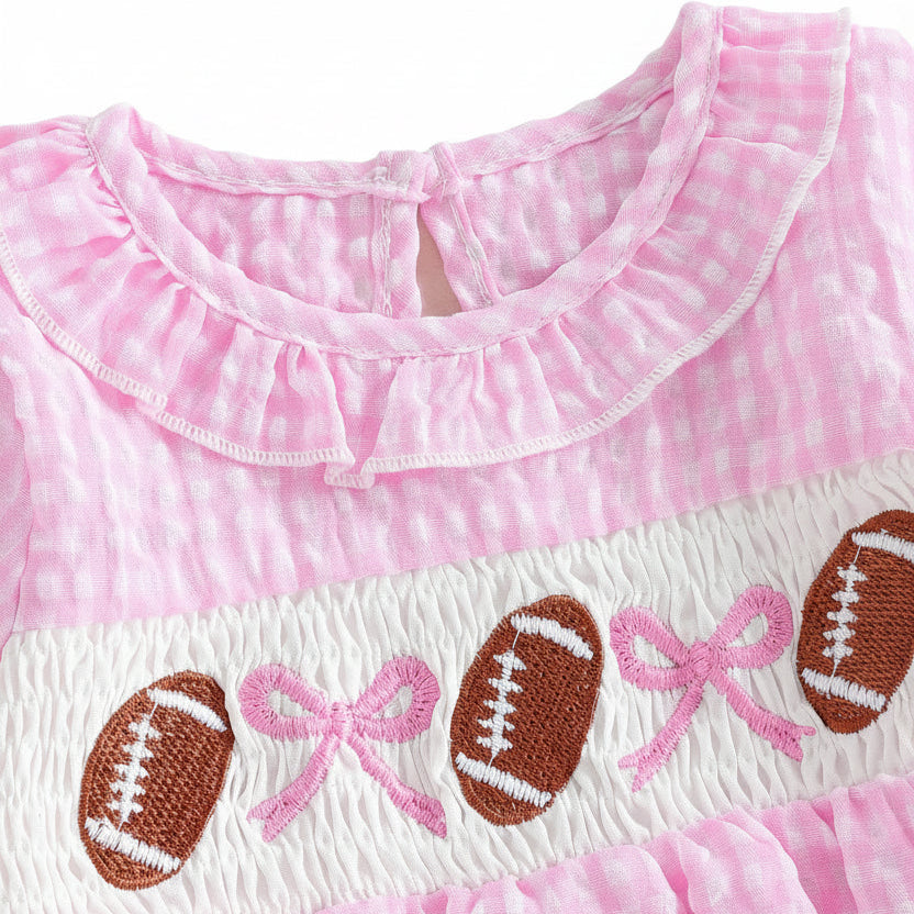 Close-up of the smocked chest detail on a baby girl's pink romper featuring embroidered footballs and bows.