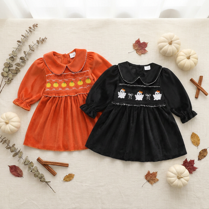 Flat lay of baby and toddler girls smocked Halloween dresses showing both the orange pumpkin and black ghost styles alongside white pumpkins and fall leaves.