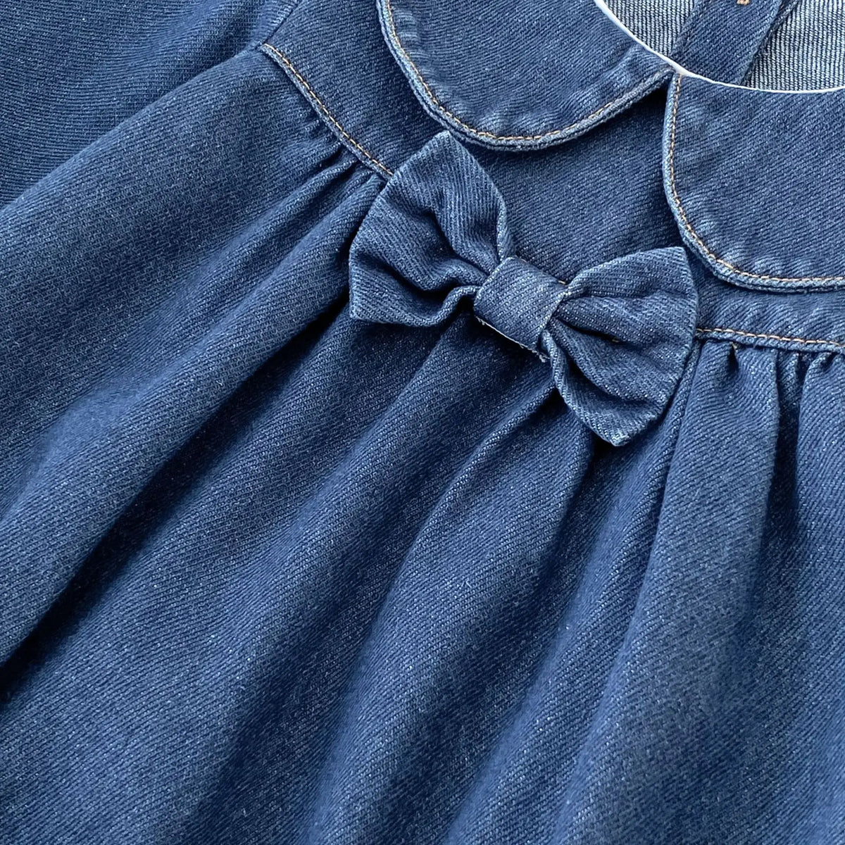 Angled close-up of soft dark blue denim material and bow accent on baby girl romper