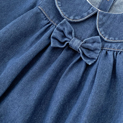 Angled close-up of soft dark blue denim material and bow accent on baby girl romper